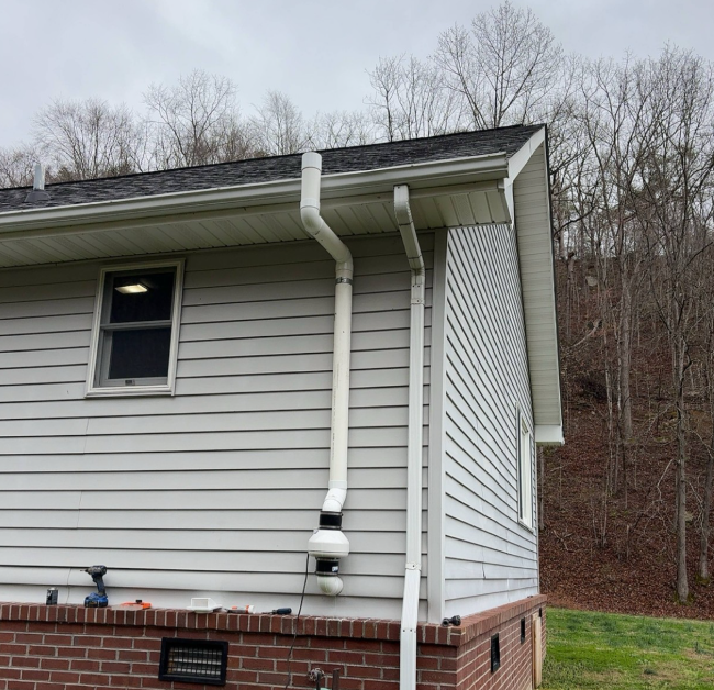 Exterior radon mitigation system with PVC vent pipe and fan installed on a home to safely vent radon gas above the roofline.