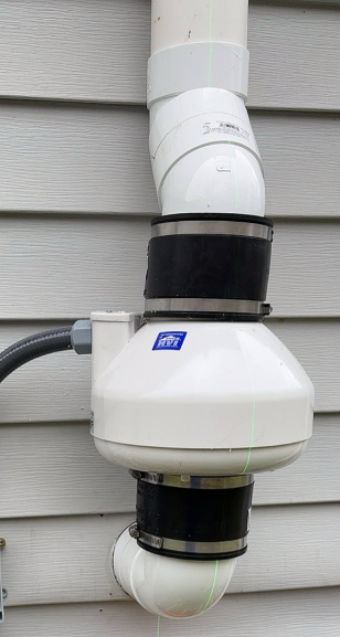 Exterior radon mitigation fan and PVC vent pipe system installed on a home to reduce indoor radon gas levels.